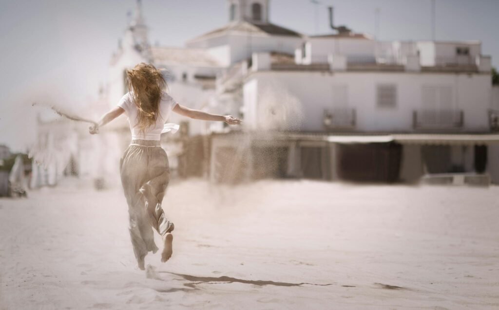 Special Offers Back view of a young woman jumping and enjoying on a sunny beach, embodying freedom and happiness.