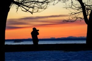 pexels photo 35507687 35507687 Silhouette of a photographer capturing a vibrant sunset by the lake.